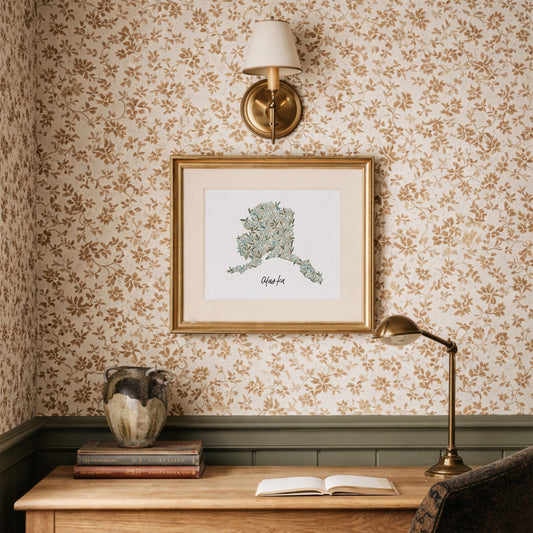 Decorative interior with floral wallpaper, framed Alaska state floral watercolor artwork, and a lamp.