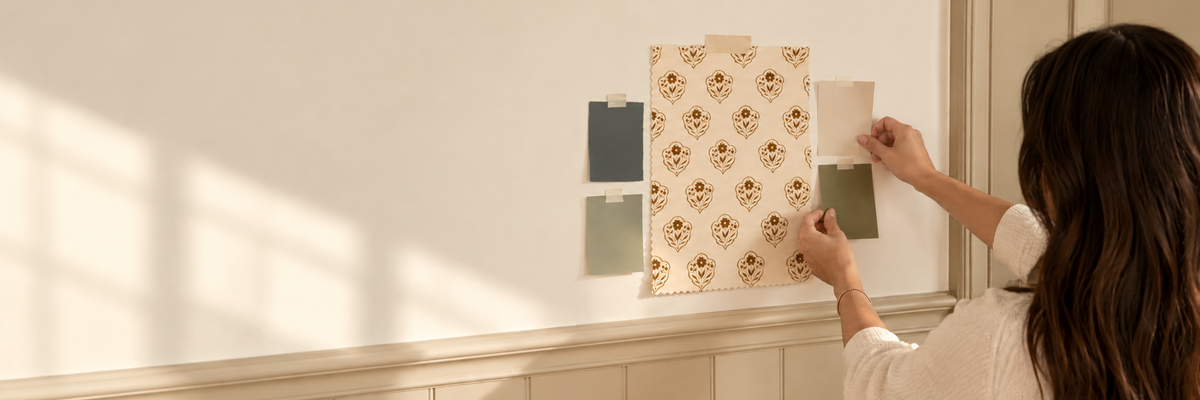 woman with brown hair holding up paint chips next to wallpaper on wall