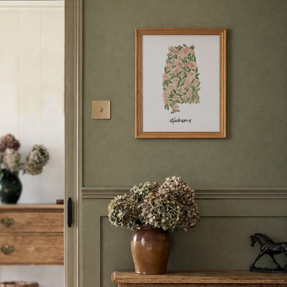 Framed floral artwork on a green wall with a vase of flowers below.