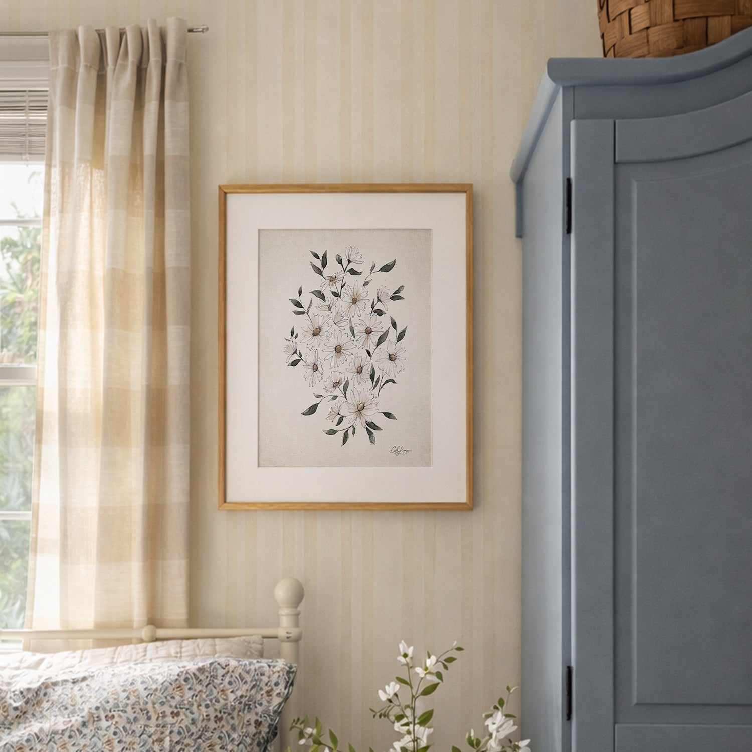 Framed April daisy birth flower watercolor art print in soft neutral tones on a wall next to a window with curtains and a blue gray cabinet.