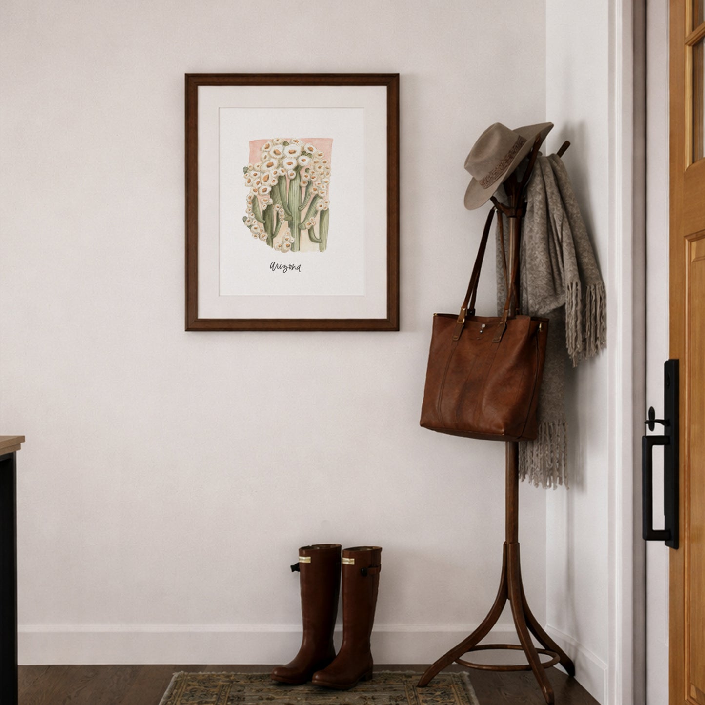 Entryway with a coat rack, boots, and framed Arizona state flower Saguaro Cactus Blossom watercolor art print framed on a wall.