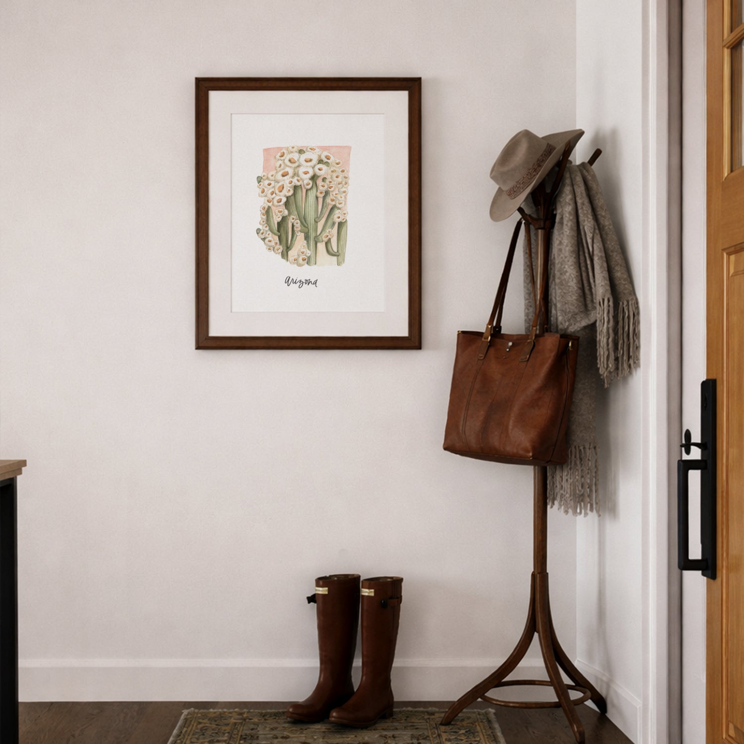 Entryway with a coat rack, boots, and framed Arizona state flower Saguaro Cactus Blossom watercolor art print framed on a wall.