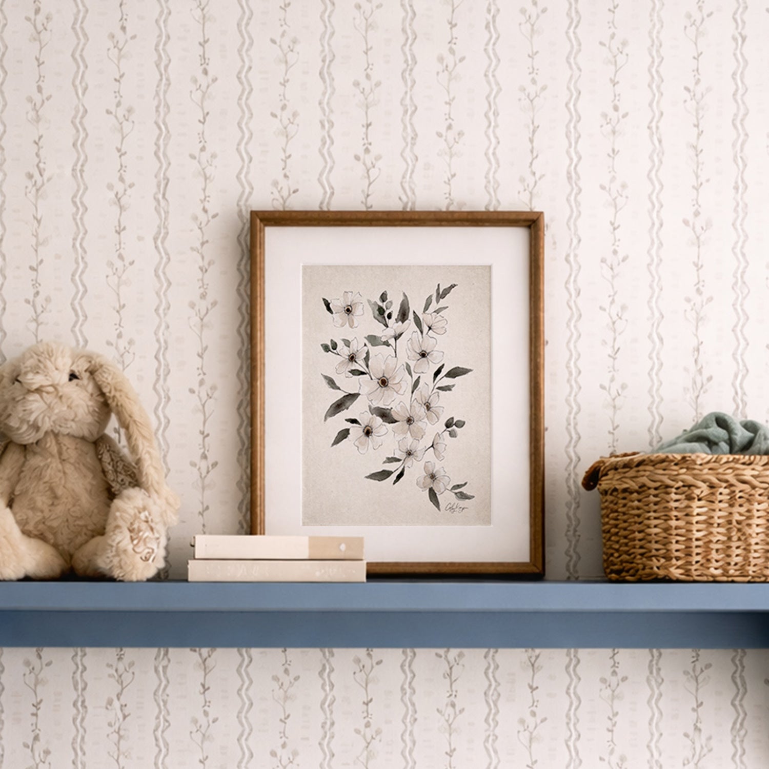 Framed February violet birth flower watercolor art print on a shelf with a teddy bear and basket against a patterned wall.