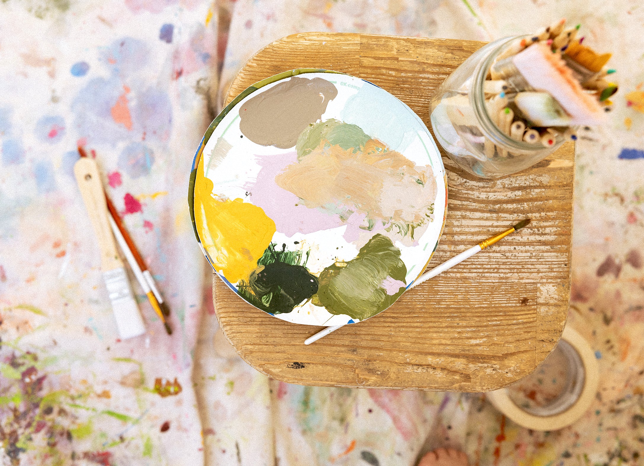 Round palette with artistic design on a wooden surface with paintbrushes and a jar.